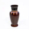 A high-gloss brown and amber drip-glaze ceramic vase holding a small green plant