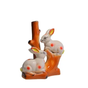 Hand-painted ceramic figurine of two white rabbits with red polka dots sitting on a brown tree trunk