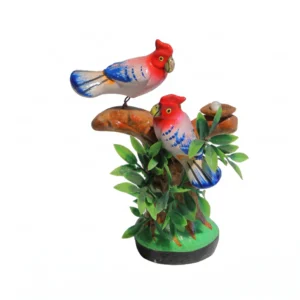 A colorful hand-painted figurine of two red and blue birds perched on a tree trunk with a nest and green leaves
