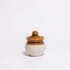 A small, 150ml handcrafted ceramic pot jar with a glossy brown lid and top and a cream-colored base, isolated on a white background.