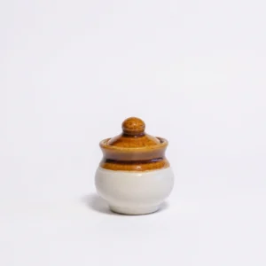 A small, 150ml handcrafted ceramic pot jar with a glossy brown lid and top and a cream-colored base, isolated on a white background.