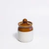 A small, handcrafted ceramic salt jar with a deep brown glazed top and cream base, standing on a white background with its matching lid.