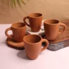 A collection of four handcrafted red terracotta mugs by Vins Art House arranged on a white and wooden surface.