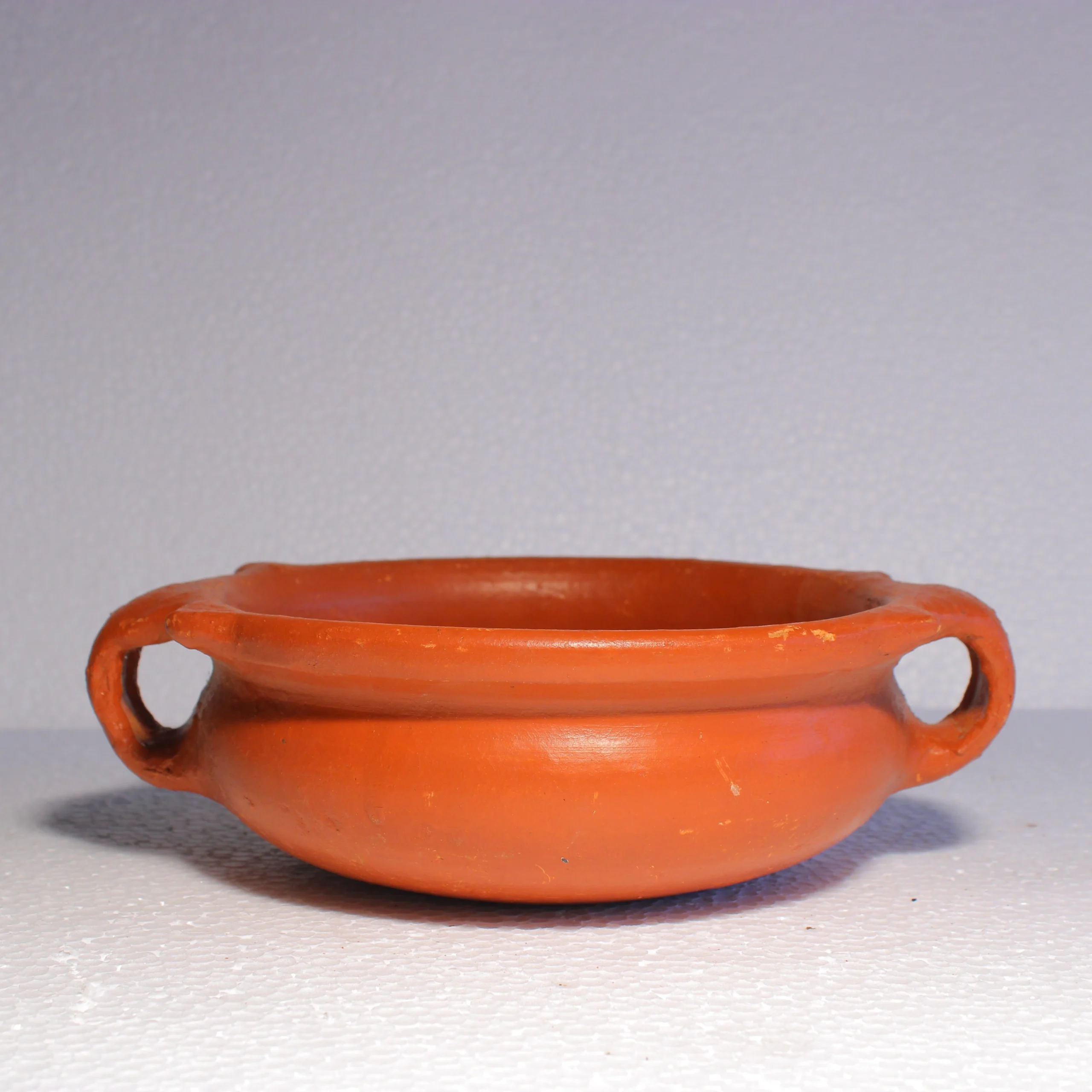 Side view of a handcrafted red terracotta uruli style chatti showing integrated clay handles.